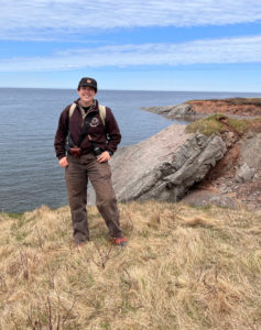 Madison Matthews, geology grad, standing on seaside cliff in hiking gear
