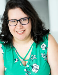 Indra has shoulder-length dark hair with glasses, wearing a green dress
