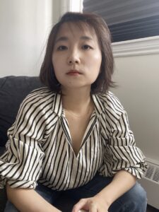 Yuan sits leaning forward wearing a button down black and white striped shirt