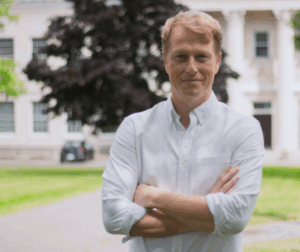 Alex wears white shirt and stands outside with the White House behind him