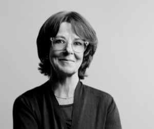 Laura has short brown hair and is wearing glasses. She stands against white background. photo is black and white