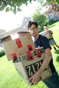 light skinned male student poses in Quad while carrying two large boxes