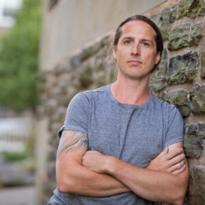 Photo of David Huebert, arms crossed, leaning against stone wall