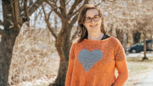 Susan Leblanc, wearing a sweater with a heart on it near a tree.