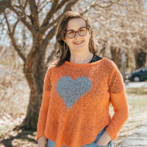 Susan Leblanc, wearing a sweater with a heart on it near a tree.