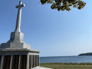 picture of memorial with cross and plaques with the harbour opening in the background