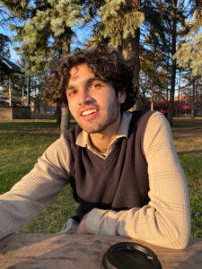 Khalil Tuff sitting in sun at picnic table with trees in background