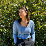 Chase Fitzgerald standing with hands in pockets looking off to her right - standing in front of rhododendron bush in King's Quad