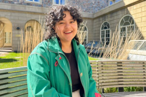 Class of 2023 Valedictorian Sam Sharp sits on bench in Wilwerth Garden on sunny day