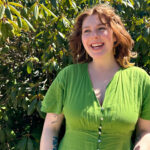Portrait of Samantha Sumner smiling and standing in front of rhododendron bush.