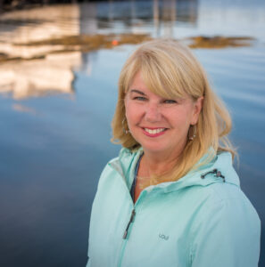 Pic of Sherri Aikenhead standing with water and reflections behind her.