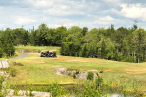 golf course with 2 golf carts sitting in background - trees on both sides of fairway