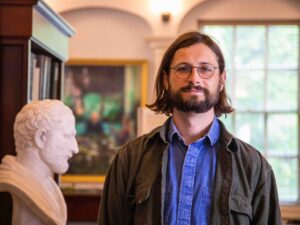 Matthew stands in the King's Library with a bust on his right side and a window over his shoulder.