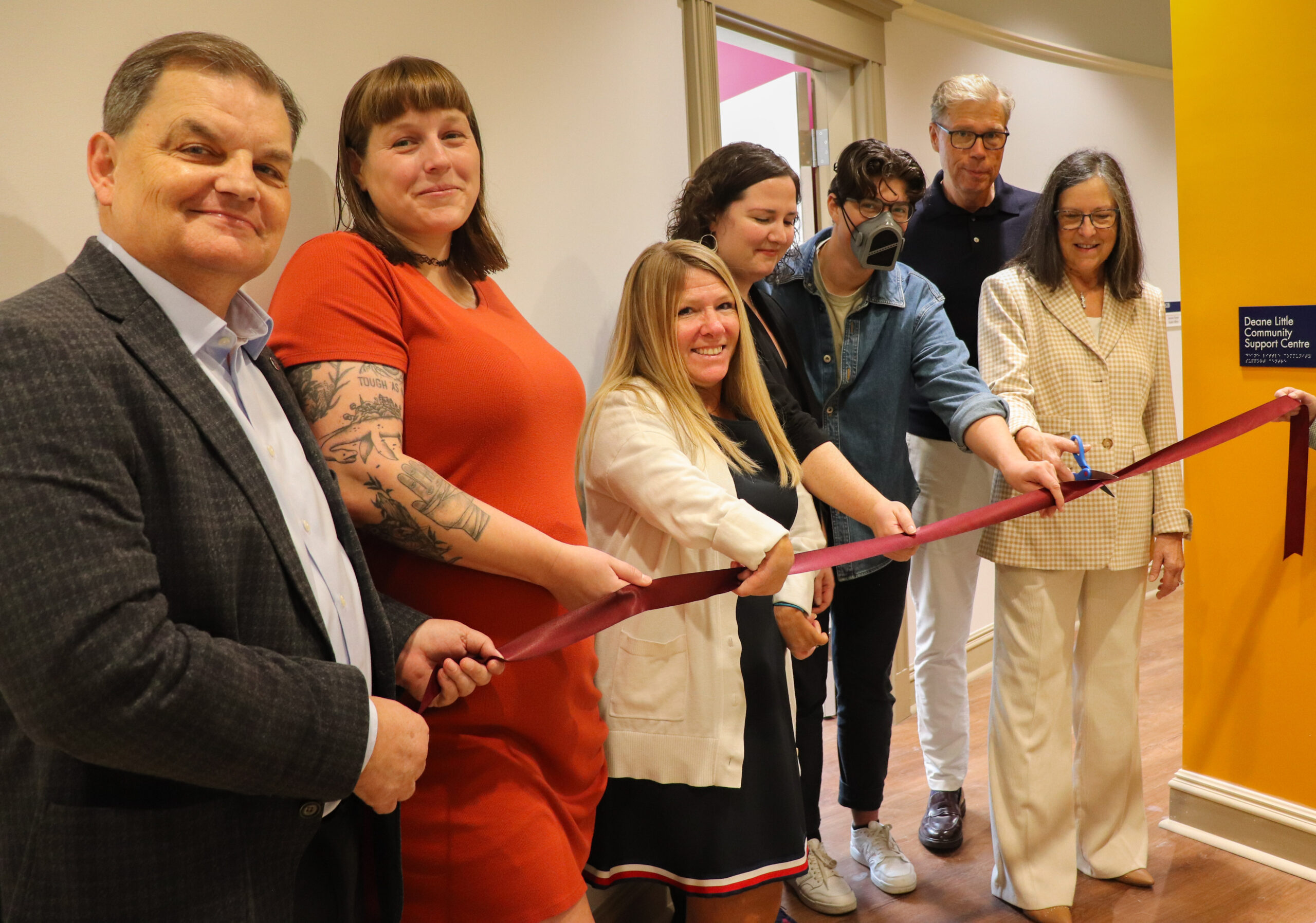 William Lahey, Jordan Roberts, Michelle Mahoney, Katie Merwin, Isaac Wright, Bob Little and Debra Deane Little hold a red ribbon as Debra cuts it in the new Deane Little Community Support Centre.