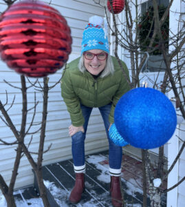 Jona Brewer crouching and looking at camera thru christmas baubles hanging on tree in foreground