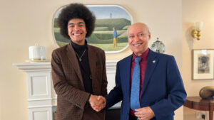 Jayden shakes hands with Gordon Earle, both smiling to camera, in front of the fireplace in the President's Lodge.