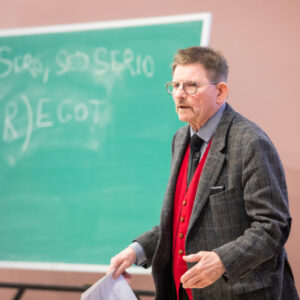 Assoc. Prof. Tom Curran delivering his final lecture stands in front of chalkboard and speaking to students.