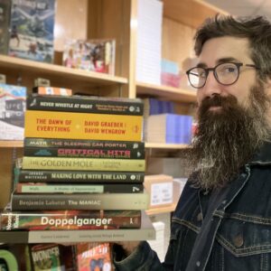 Paul McKay stands holding a pile of books in the King's Co-op Bookstore