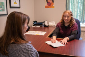 peer advisor at desk sits across from student. advisor is pointing to king's course guide.