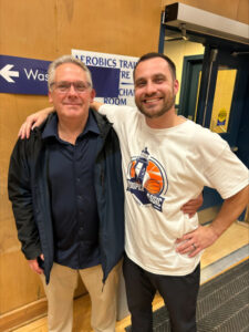 Neil Hooper stands next to Coach Luc Stevenson who has his right arm around Neil's shoulders.