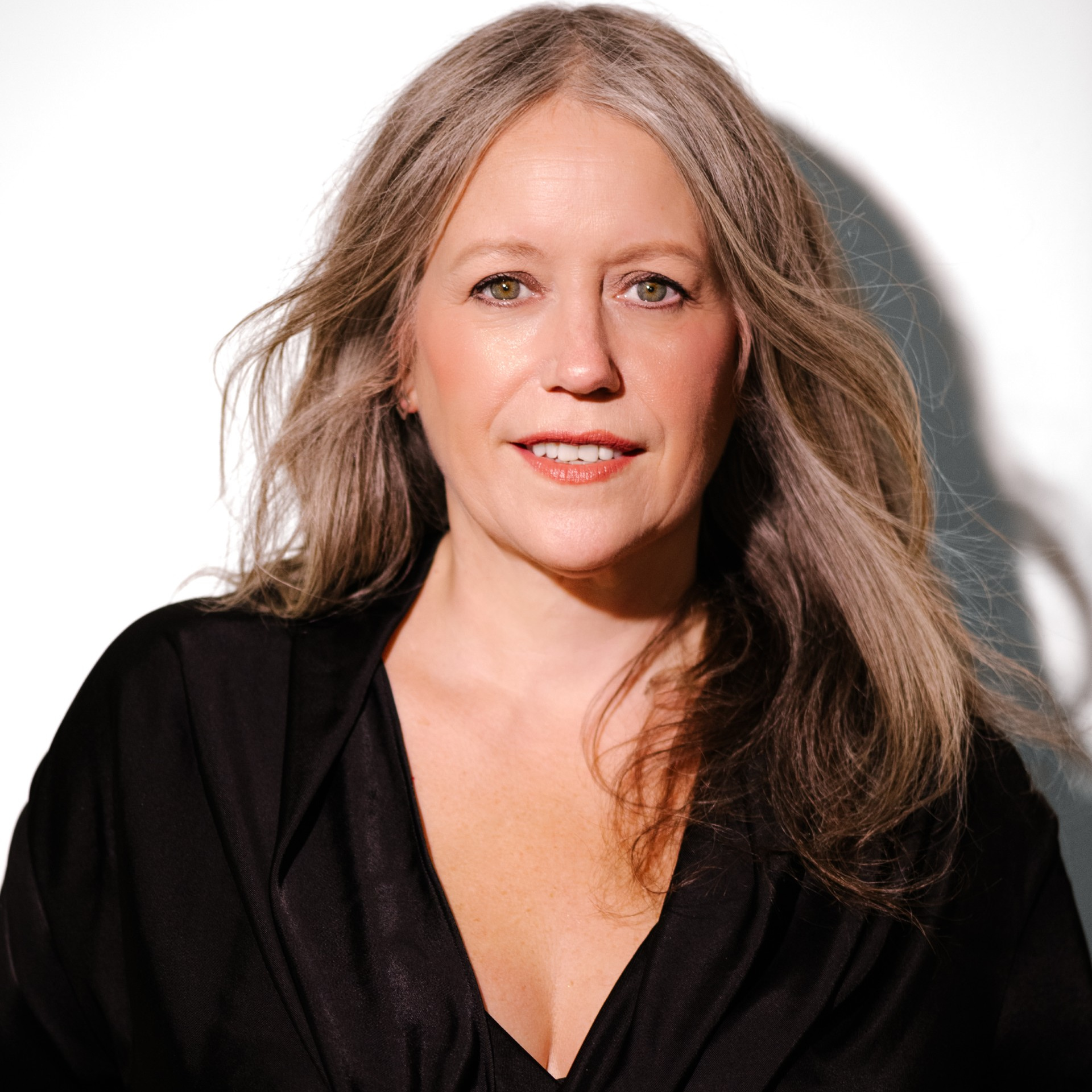 Sherry wears a black v neck, has long fair hair and is standing against a white background