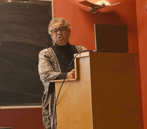 Louise stands at lectern speaking to audience