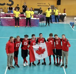 goalball team stands in red jerseys on turquoise court holding Canadian flag