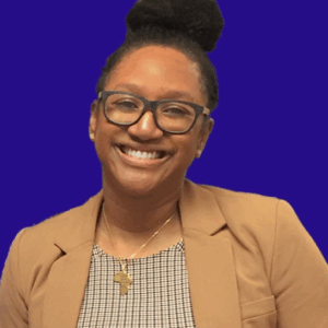 Melina has her hair up in a high bun, wears glasses. She has a tan blazer on over a black/tan/white gingham check shirt