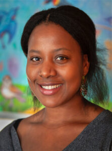 Iryn smiles to camera with painted birds on blue wall in background.