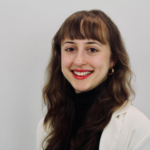 head shot of Lucretia against neutral background. Long reddish-brown hair with bangs and smiling to camera