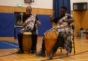 drummers from Kwestomar sit before their drums in gymnasium during performance for African Heritage Night.