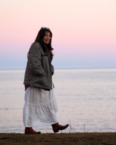 Petra walks on the shoreline, water and dusky sky in background.