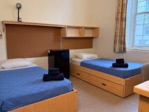 Twin beds with blue coverlets and window to right in Alex Hall.