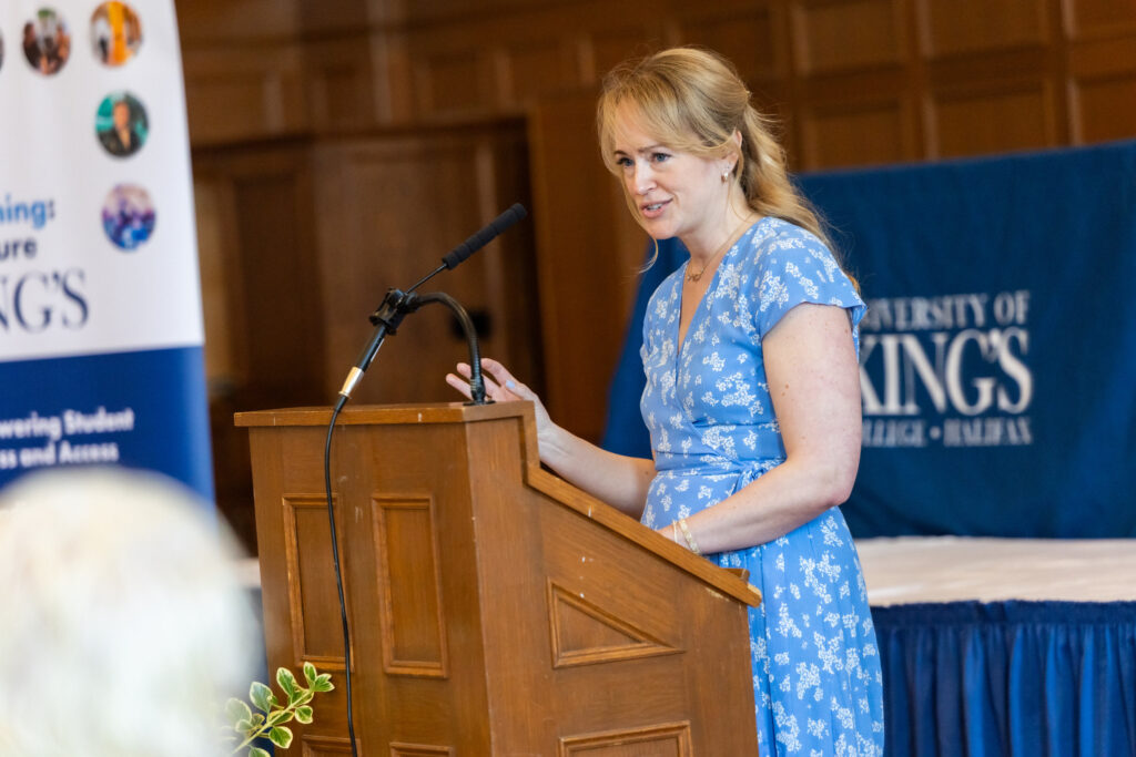 Jenn Thornhill Verma stands at podium speaking to audience at Alumni Day